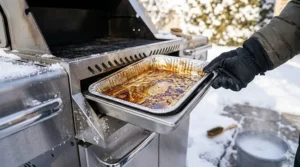 Illustration showing how to empty and clean a BBQ grease tray to prevent freezing and pests in winter.