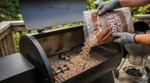 Close-up of hardwood pellets being poured into a pellet smoker hopper for a consistent outdoor cooking experience.